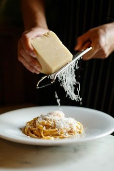 a person grating cheese on top of spaghetti