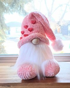 a pink stuffed animal with white fur and hearts on it's face sitting in front of a window