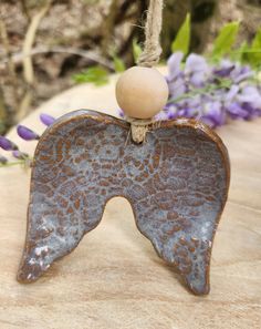 a ceramic angel ornament hanging from a rope with purple flowers in the background