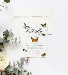 a wedding card with butterflies on it next to flowers and greenery in front of a white background