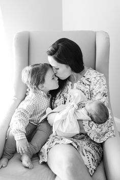 a woman sitting on top of a chair holding a baby and kissing her face with the other