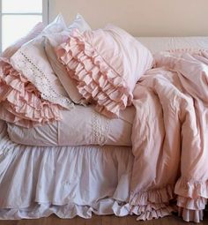 a bed covered in pink ruffled sheets and pillows