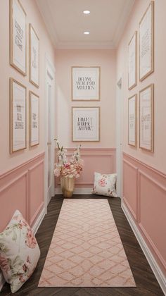 a hallway with pink walls and framed pictures on the wall, along with two flowered pillows