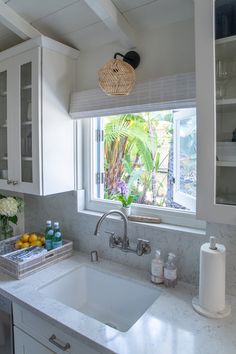 a kitchen with white cabinets and marble counter tops, along with a window over the sink