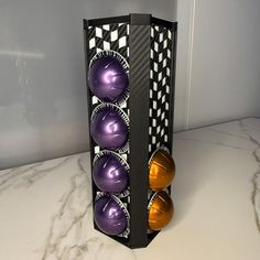 three metallic balls in a black box on a marble counter top next to an orange and purple vase