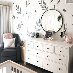 a baby's room with a dresser, mirror and wall decals on the walls