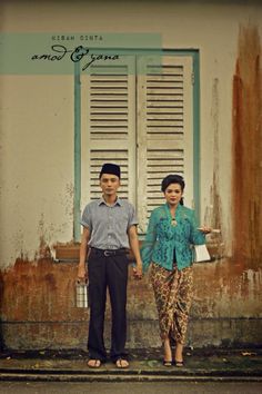 a man and woman standing in front of a building with shutters on the windows