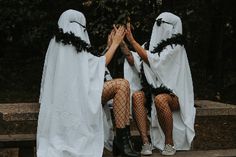 three women dressed in white are sitting on a bench and covering their faces with hands