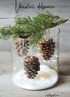 some pine cones are in a glass jar with snow on the bottom and one is hanging from