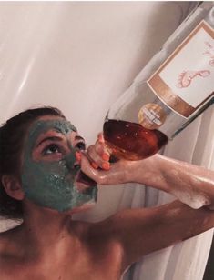 a woman is taking a shower with her face covered in facial mask and holding a bottle of booze