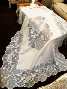 a white table cloth with an intricate lace design on it sits in front of a couch