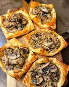 small pizzas with mushrooms on them sitting on a cutting board