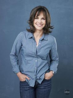 a woman standing in front of a blue wall with her hands on her hips and smiling