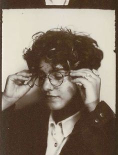 an old black and white photo of a woman wearing glasses with curly hair in front of her face