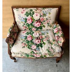 an old fashioned chair with floral fabric and wood trimmings, sitting against a wall