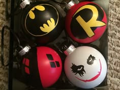 four ornaments with batman symbols on them are in a black box and one is red, the other is white