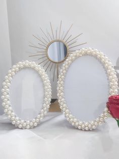 two oval mirrors with pearls and a rose on the table in front of a mirror