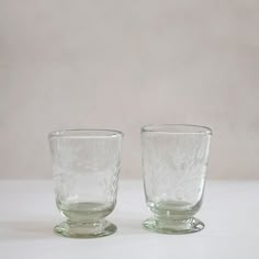 two glass cups sitting next to each other on a white tableclothed surface,