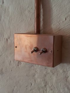 a copper light switch mounted to the side of a white wall with metal fittings