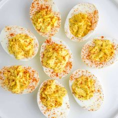 deviled eggs on a white plate with mustard sprinkled on them and seasoning