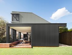 an outdoor area with wooden decking and black corrugated cladding on the side of a house