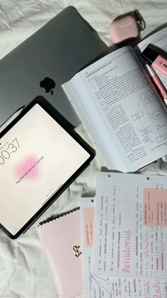 an open laptop computer sitting on top of a white bed next to papers and other items