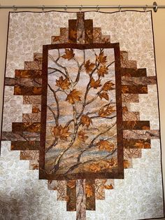 a quilted wall hanging with a tree on it's side and leaves in the middle