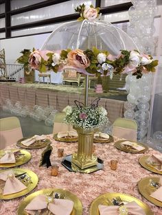 the table is set with gold plates and pink napkins, silverware, and an umbrella shaped centerpiece