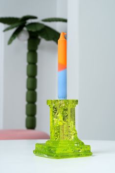 a green candle holder with an orange, blue and yellow candle sticking out of it