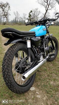 a blue and black motorcycle parked on top of a grass covered field with trees in the background