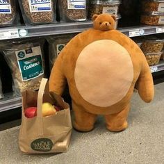 a large stuffed bear standing next to a bag full of apples and nuts in a grocery store