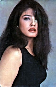 an old photo of a woman with long hair wearing a black dress and pearl earrings