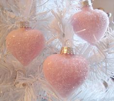 three pink ornaments are hanging from a white christmas tree