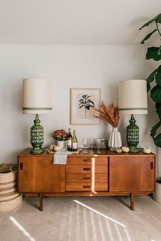 a living room with two lamps on top of a wooden cabinet next to a plant