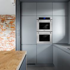 a kitchen with two ovens and a wooden counter top in front of a brick wall