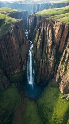 an aerial view of a large waterfall in the middle of a valley with green grass