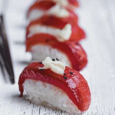 there are several sushi rolls with toppings lined up on a white table next to a fork