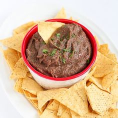 a red bowl filled with black bean dip surrounded by tortilla chips on a white plate