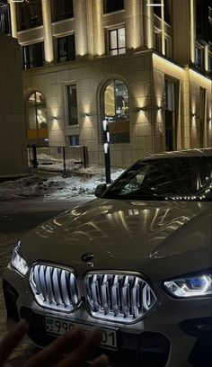 a bmw car parked in front of a building at night with its headlights turned on