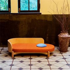 an orange couch sitting next to a brown vase on top of a tiled floor in front of a window