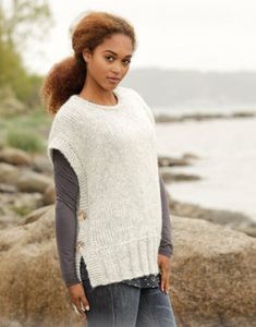 a woman is standing by the water wearing a sweater and jeans with buttons on it