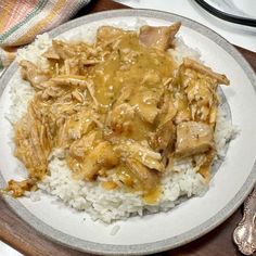 a white plate topped with rice and meat covered in gravy on top of a wooden table