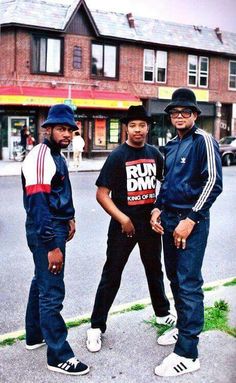 three young men standing next to each other on the side of a road with buildings in the background