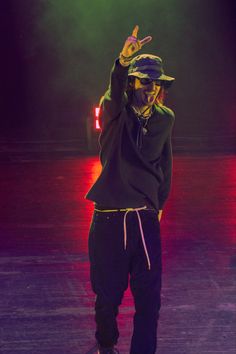 a man standing on top of a stage with his hand up in the air while wearing a hat