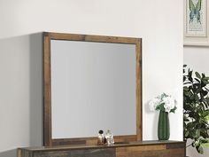 a mirror sitting on top of a wooden dresser next to a vase with white flowers