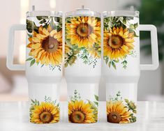 three sunflowers painted on the side of two white coffee mugs sitting on a table