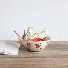 a bowl filled with fruit sitting on top of a wooden table next to an open book