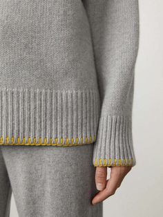 a close up of a person wearing a gray sweater and pants with yellow trims