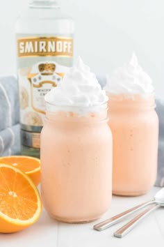 two mason jars filled with whipped cream next to an orange and a bottle of smirnoff