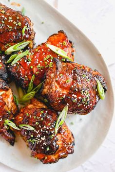 a white plate topped with meat covered in sesame seeds and garnished with green onions